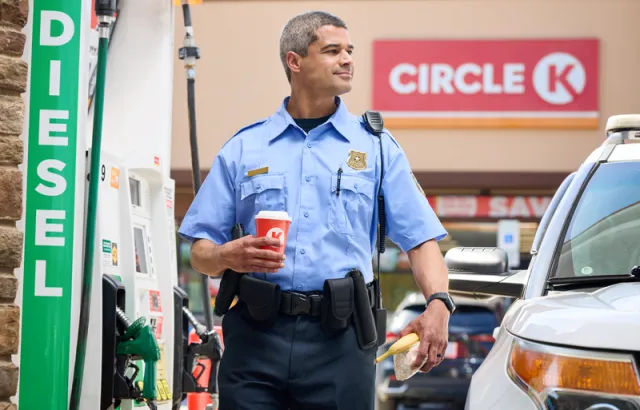 Police officer walking by a Circle K station with a coffee in hand