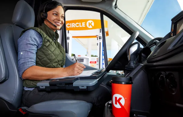 Business woman sitting in her vehicle outside a Circle K station, talking to Circle K Pro team using her headset